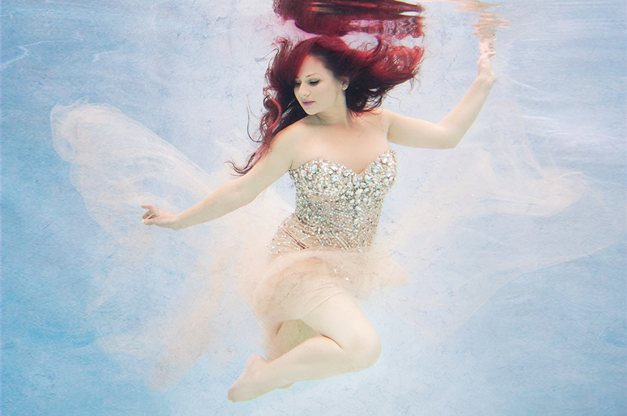 A gorgeous red headed woman wearing a rhinestone evening gown underwater.